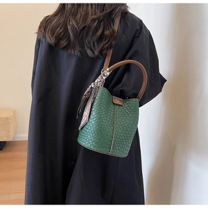 Detail of dark green crocodile embossed bucket bag with printed silk scarf on handle