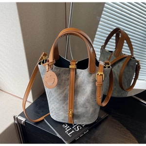 Detail of grey fabric bucket bag with brown leather straps and a smiley face charm