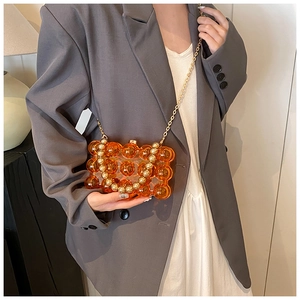 Model wearing a vibrant orange acrylic crossbody bag with bubble embossed texture and chain