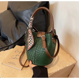 Detail of green woven texture bucket bag with silk scarf and logo on a stone base