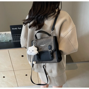 Detalle del bolso bandolera gris y negro con un suave colgante de felpa de nube blanca