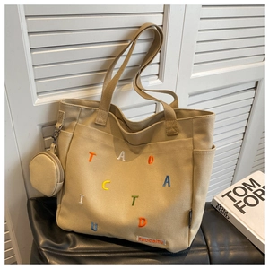 Detail of beige canvas tote bag with colorful letter embroidery and small round pouch
