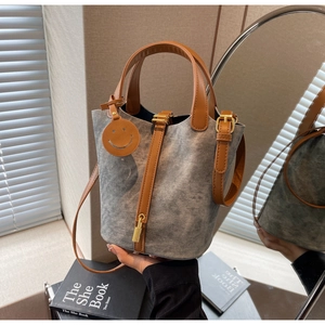 Detail view of denim bucket bag with brown leather straps and gold metal lock charm