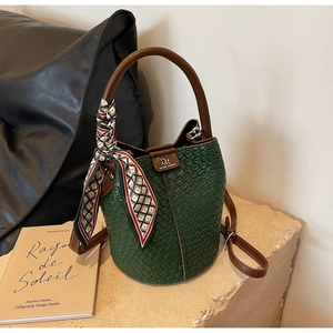 Detail of dark green woven bucket bag with brown leather handles and a silk scarf accent