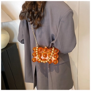 Detail of a transparent orange wave evening bag with gold chain strap on grey blazer