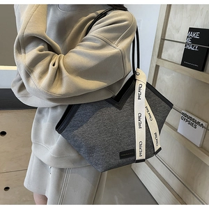 Détail du sac cabas gris foncé avec sangle tissée et bordure en cuir porté par un modèle