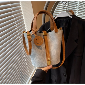 Detail of light blue denim bucket bag with brown leather trim and gold padlock charm