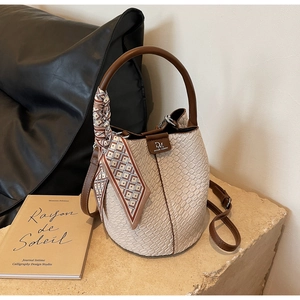 Detail of beige bucket bag with woven texture, round handle, and vintage scarf accessory