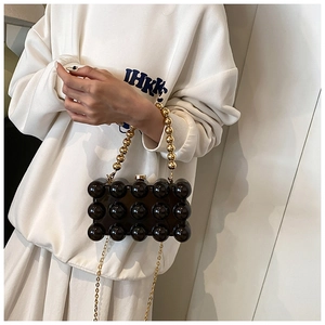 Detail of black acrylic evening bag with beaded texture and gold chain worn by model