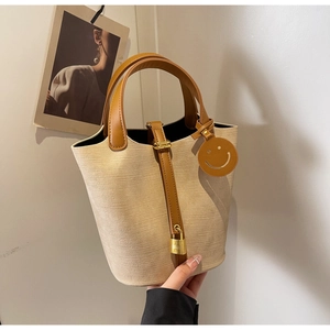 Detailed close-up of beige woven bucket bag with brown leather handle and H-buckle