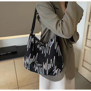 Detail of black tote bag with colorful embroidery and leather logo on shoulder strap