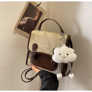 Detalle de bolso de lona bicolor con correas de cuero marrón y colgante de peluche