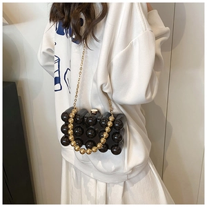 Detail of black acrylic shell bag with pearl texture and gold chain strap on model