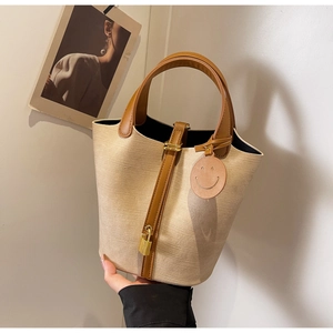 Detail of beige bucket bag with brown leather trim, golden padlock, and smiley tag