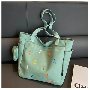 Detail of light green canvas tote bag with colorful embroidery and side coin pouch