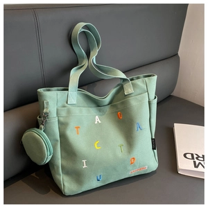 Detail of light green canvas tote bag with letter embroidery and round coin purse
