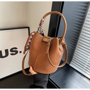 Close-up of brown woven bucket bag with silk scarf handle and silver metal buckle