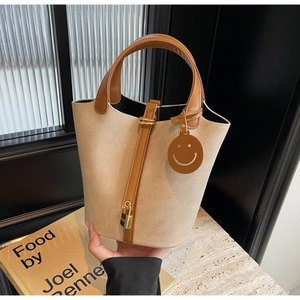 Close-up of canvas bucket bag with brown leather trim and golden metal lock detail