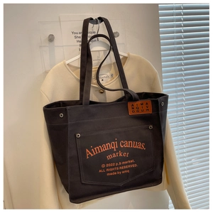 Detailed close-up of dark grey canvas tote bag featuring silver rivets and orange leather patch