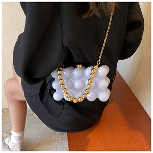 Close-up of a white bubble texture handbag featuring a chunky gold bead handle and metal chain