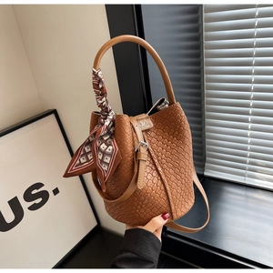 Detail of a brown woven bucket bag with silk scarf on handle and metallic RM logo