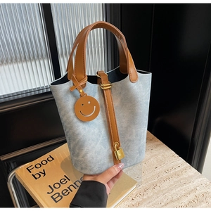 Macro shot of light blue denim bucket bag with brown leather handles and gold lock detail