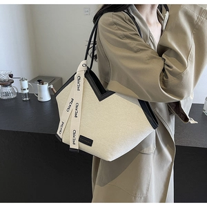 Détail du cabas en toile avec passepoil contrasté et sangle de marque porté par modèle