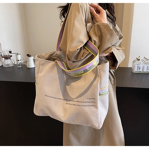 Detail of canvas tote bag showing colorful three-tone striped straps and slogan print