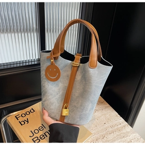 Detail of light blue denim bucket bag with brown leather handles and golden lock charm