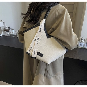 Détail du sac cabas en toile crème avec garniture en cuir noir et breloque décorative