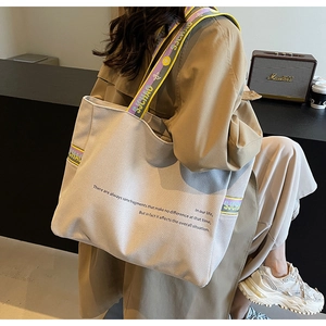 Close-up of canvas tote bag featuring striped shoulder straps and minimalist typography
