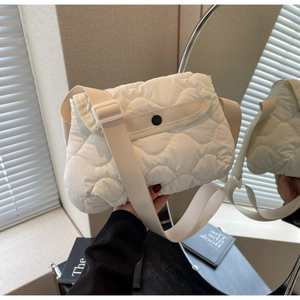 Detail of white quilted puffer crossbody bag with black buckle and wide shoulder strap