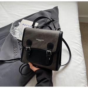 Detalle de mochila de lona gris y cuero negro con hebillas de metal sobre escritorio