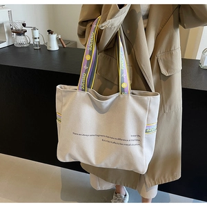 Detail of beige canvas tote bag with purple and yellow stripes held by a model in a trench coat