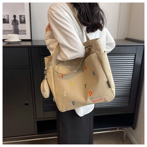 Detail of khaki canvas tote bag featuring colorful embroidered letters and small coin purse