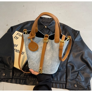 Detail of denim bucket bag with brown leather handles and gold padlock accessory