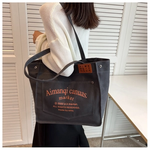 Detail view of large dark grey canvas tote with orange lettering and leather tag