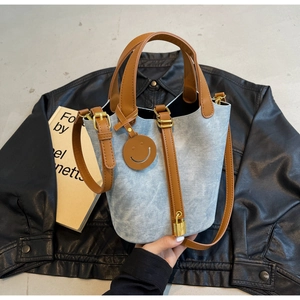 Detail of blue denim bucket bag with brown leather trim and gold hardware accents