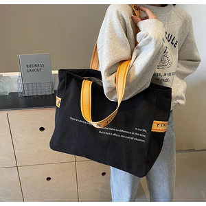Close-up of black canvas tote bag featuring orange striped straps and white quote print