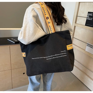Detail of black canvas tote bag showing decorative wide shoulder strap and white text print