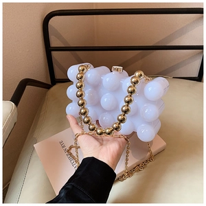 Chic cream clutch bag with bubble texture and gold beaded handle shown in hand