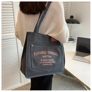 Detail view of dark grey canvas tote bag with front snap pocket and orange lettering