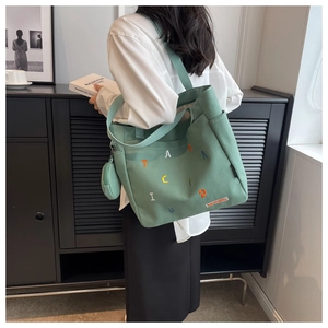Detail of green canvas tote bag featuring multi-colored letter embroidery and wide strap