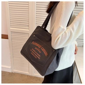 Lifestyle view of large black canvas tote bag with orange lettering and metal buckle