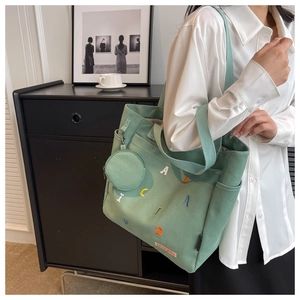 Detail of light green canvas tote with embroidered letters and small round purse attachment