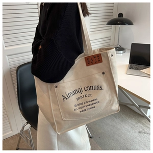 Detail of beige canvas tote bag with front pocket and rivet accents for daily commuting