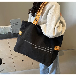 Detail of large black canvas tote bag featuring yellow jacquard straps and casual style
