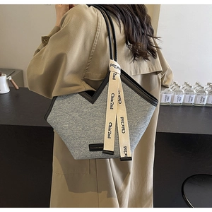 Détail du sac cabas en denim gris avec bordure en cuir noir et ruban logo de marque