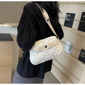 Detailed view of a white quilted crossbody bag with adjustable strap worn on person