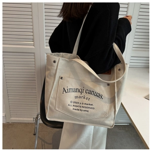 Detail of off-white canvas tote bag with front pocket, metal snap and letter print